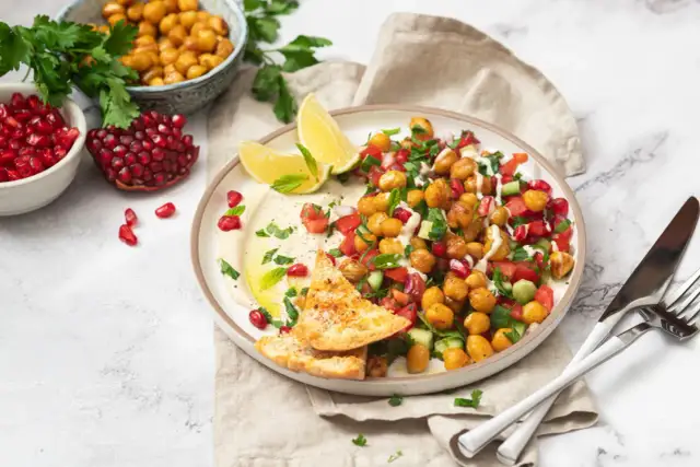 Bunter Kichererbsen Salat mit Granatapfelkernen, Tomaten, Gurken und Hummus, garniert mit Minze und serviert mit Pitabrot.