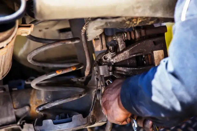 Mechanik przy pracy nad sprężyną amortyzatora. Dowiedz się, jak ścisnąć sprężynę amortyzatora domowym sposobem.