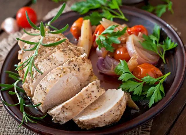 Pokrojony pieczony filet z kurczaka z pieczonymi pomidorkami, cebulą i ziołami.