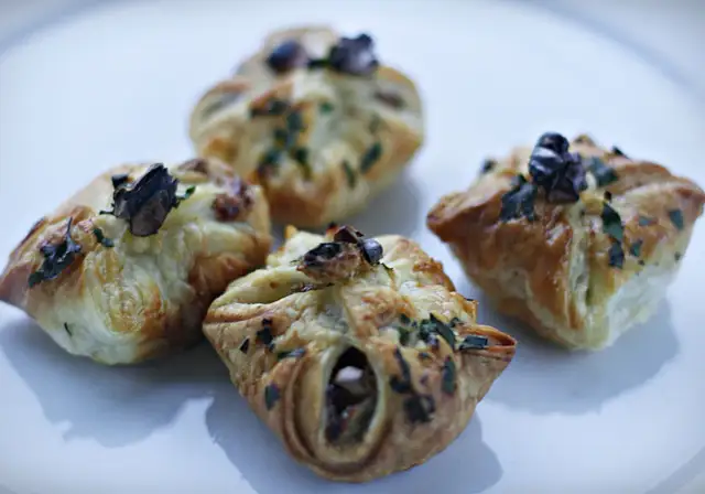Cztery apetyczne paczuszki z ciasta francuskiego z gruszkami i gorgonzolą, posypane ziołami.