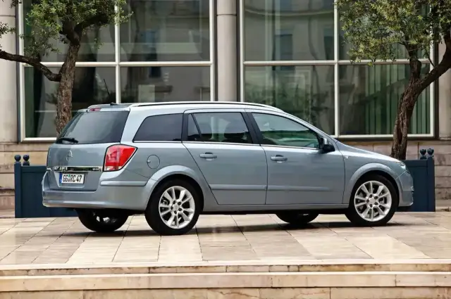 Srebrny Opel Astra H kombi stoi przed nowoczesnym budynkiem.