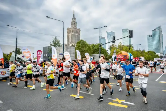 Uczestnicy biegną w maratonie, pokonując jego długość. W tle Pałac Kultury i Nauki.