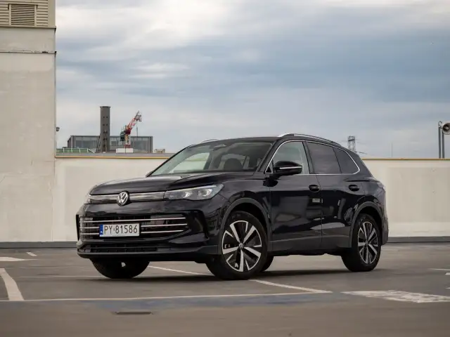 Czarny Volkswagen Tiguan na parkingu. W tle budynki i dźwig. Wiele osób szuka volkswagen tiguan opinie przed zakupem.