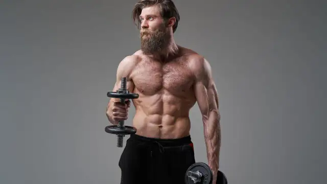 Mężczyzna z imponującą brodą wykonuje ćwiczenia na biceps, trzymając hantle do hammer curls.