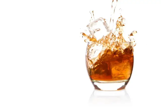 Bursztynowa whisky z lodem rozpryskuje się w szkle. Czy whisky podnosi ciśnienie? To pytanie pozostaje otwarte, gdy patrzymy na ten dynamiczny obraz.