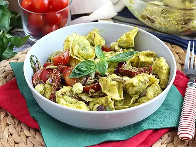 Tortellini z pesto, pomidorkami koktajlowymi i bazylią w białej misce.