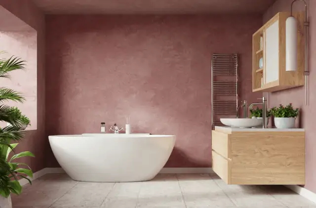 Un baño moderno con bañera independiente y tocador de madera. Las paredes de color rosa empolvado y las plantas aportan un toque acogedor a estos baños rústicos.