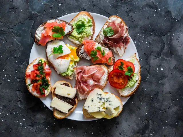 Talerz pełen pysznych sznytek: z łososiem, awokado, jajkiem w koszulce, szynką parmeńską, pomidorami i serami.