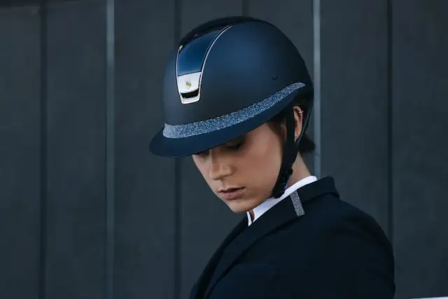 Elegancki kask marki kask, ozdobiony brokatową taśmą, noszony przez kobietę w czarnym żakiecie.