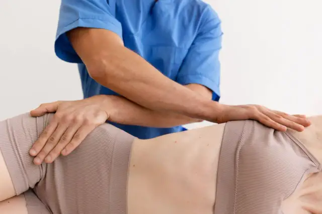 Fizjoterapeuta wykonuje masaż biodra, łagodząc mrowienie. Dłonie terapeuty obejmują okolicę biodrową pacjentki.