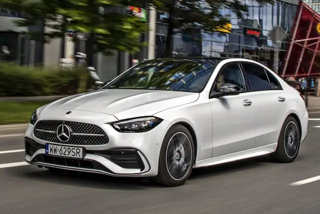 Biały Mercedes Klasy C w ruchu miejskim, widok z przodu i z boku.