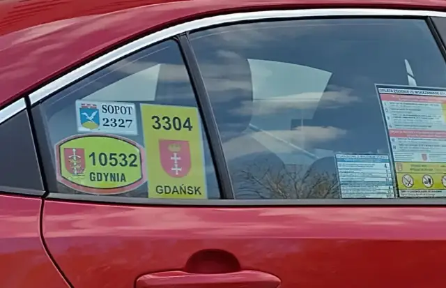 Naklejki taksówkarskie z numerami i herbami miast: Sopot, Gdynia, Gdańsk na czerwonym samochodzie.