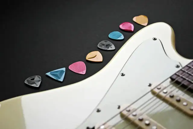 Różnokolorowe kostki do gitary elektrycznej leżą obok białej gitary. Wybierz odpowiednią, by zacząć naukę, jak nastroić gitarę elektryczną.