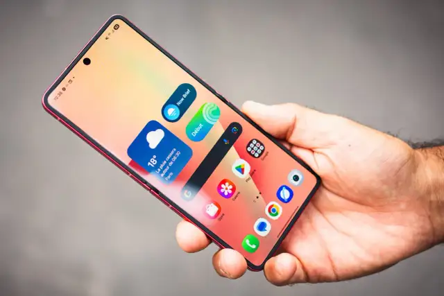 Main d'homme tenant un smartphone rouge, affichant des widgets météo et des icônes d'applications, dont Samsung Internet.