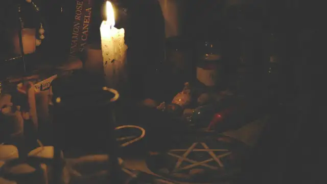 Mroczna atmosfera, płonąca świeca, książka z napisem "Cinnamon Rose", muszelki i pentagram. Czy pentagram jest zły? To zależy od intencji.