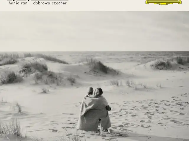 Dwie kobiety otulone kocem na plaży, słuchają **Hania Rani Inner Symphonies**.
