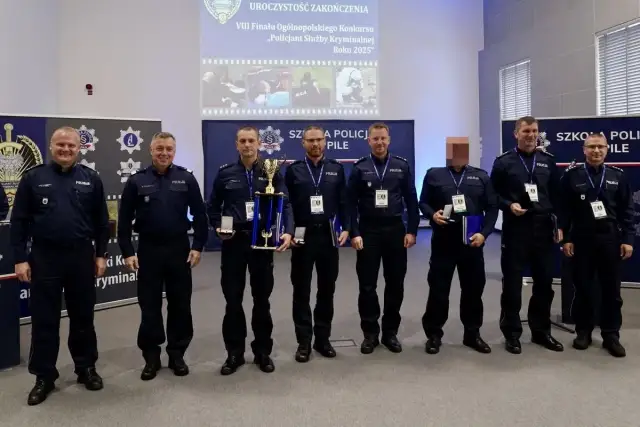 Policjanci w mundurach stoją w rzędzie, niektórzy trzymają nagrody i dyplomy.