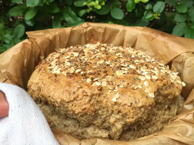 Pan de lino recién horneado, cubierto de semillas y avena, envuelto en papel de hornear.