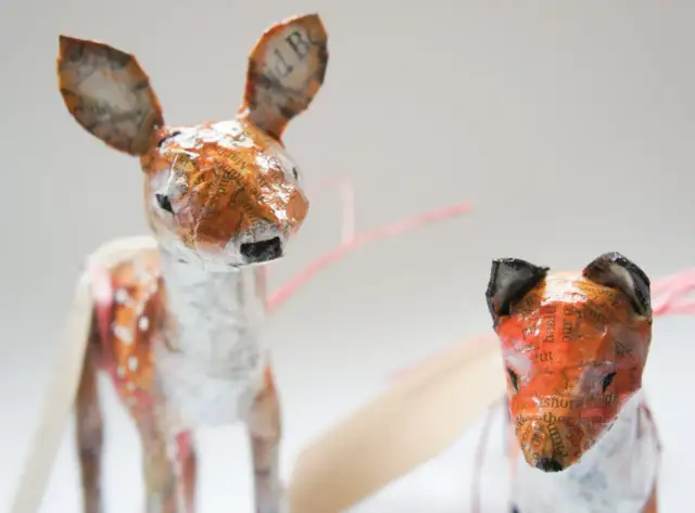 Urocze figurki z papier mache: jelonek w plamki i lis. Ich uszy zdobią fragmenty tekstu.