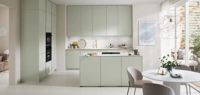 Moderna cocina verde con isla central, electrodomésticos integrados y una mesa redonda con sillas.
