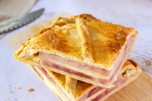 Dos porciones de empanada de jamón y queso apiladas, con masa dorada y relleno visible.