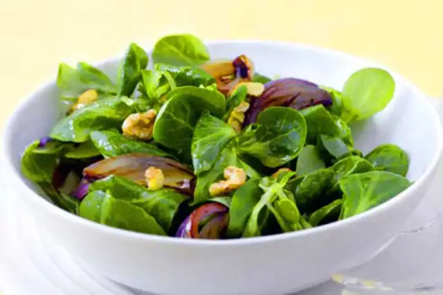 Ein frischer Feldsalat mit knackigen Zwiebeln und Walnüssen in einer weißen Schüssel.