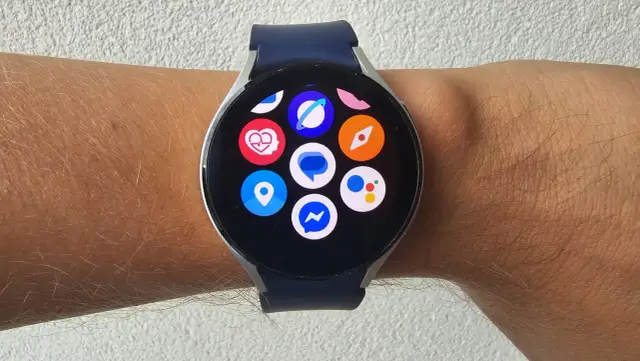 Zegarek z systemem Wear OS na nadgarstku, z widocznymi ikonami aplikacji: serce, lokalizacja, Messenger, Google Assistant i inne.