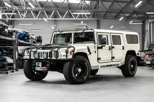 Biały Hummer H1 z potężnymi oponami i dodatkowym oświetleniem na dachu, gotowy na każdą przygodę.