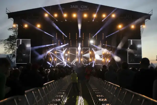 Jarocin Festiwal rozświetlony tysiącami świateł. Tłum czeka na koncert, a na scenie widać artystów.