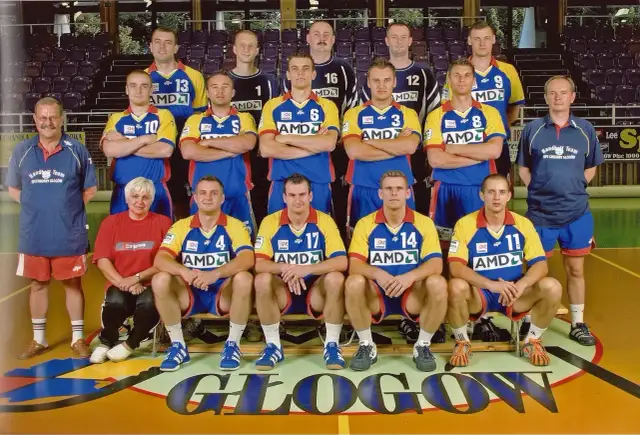 Drużyna SPR Chrobry Głogów pozuje do zdjęcia. Zawodnicy w żółto-niebieskich strojach sportowych, trenerzy i jedna kobieta.