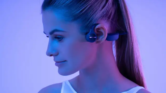 Profil d'une femme portant un casque à conduction osseuse bleu, éclairée par des lumières bleues et roses.
