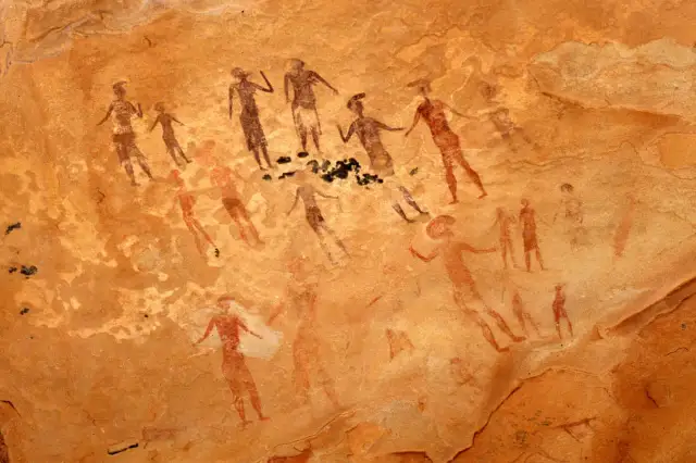 Prehistoryczne malarstwo jaskiniowe ukazuje grupę postaci ludzkich w ruchu, być może podczas rytuału lub polowania.
