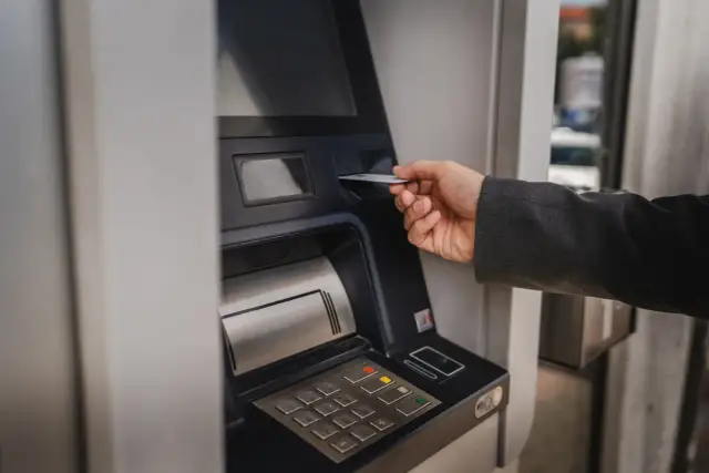Dłoń wsuwa kartę do bankomatu, by sprawdzić, ile można wypłacić.