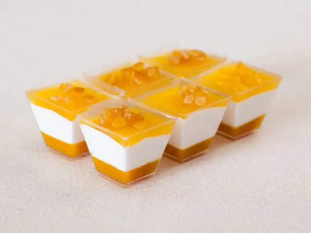 Sechs kleine Dessertgläser mit weißer Creme und Mango-Topping, garniert mit kleinen Fruchtstückchen.