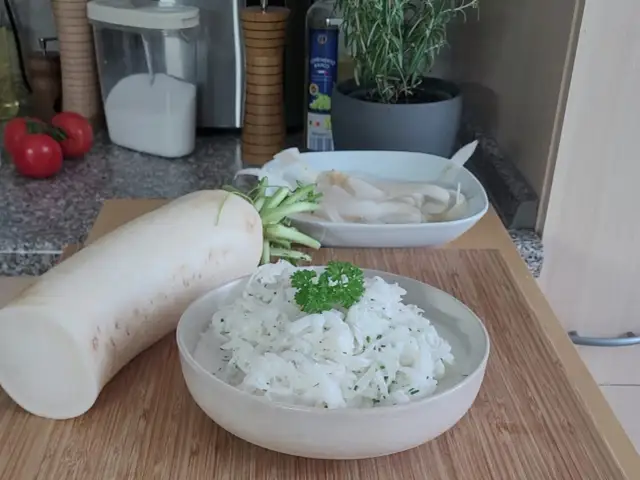 Ein frischer Rettich liegt neben einer Schüssel mit cremigem Rettichsalat, garniert mit Petersilie. Perfekt für ein leichtes Rettichsalat Rezept.