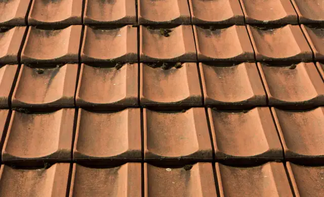 Czerwona dachówka ceramiczna, lekko porośnięta mchem. Sprawdź aktualną dachówka ceramiczna cena za m2.