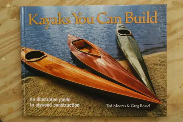 Książka "Kayaks You Can Build" pokazuje, jak zbudować kajak ze sklejki. Trzy piękne, drewniane kajaki na plaży.