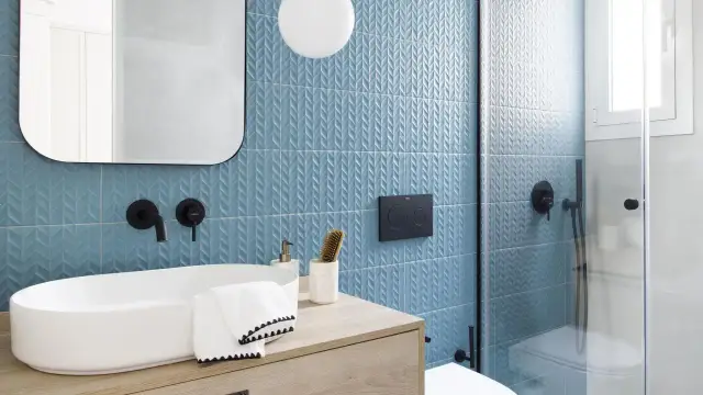 Moderno baño con azulejos azules texturizados y lavabo ovalado. Ideas para cuartos de baño pequeños: grifería negra, espejo redondeado y ducha de cristal.
