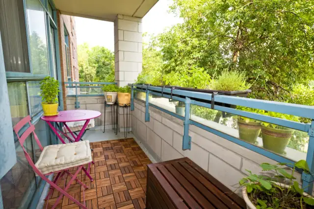 Zielony balkon z meblami i roślinami. Jak osłonić balkon w bloku? Rośliny na balustradzie i drewniana podłoga dodają uroku.