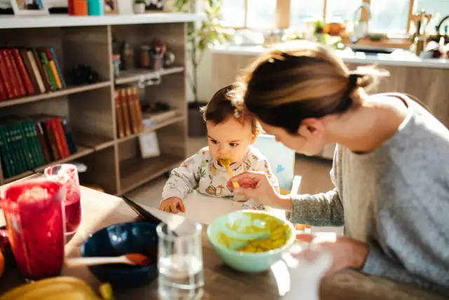 Mama karmi łyżeczką 6 miesięczne dziecko. Na stole są owoce i napoje.