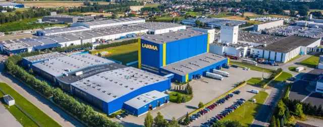 Widok z lotu ptaka na fabrykę Lakma z niebiesko-żółtymi budynkami i parkingiem.