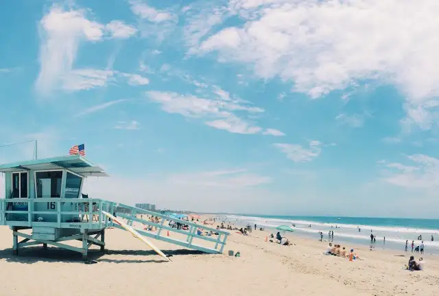 Słoneczna plaża w USA z wieżą ratowniczą i ludźmi odpoczywającymi nad oceanem. Idealne miejsce, by sprawdzić, ile trwają wakacje w USA.