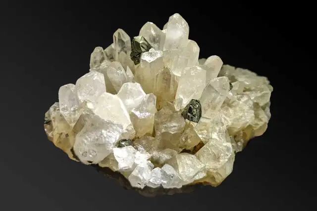 Ein Cluster aus klaren, facettierten Quarz-Kristallen mit dunklen Einschlüssen. Was ist Quarz? Ein faszinierendes Mineral!