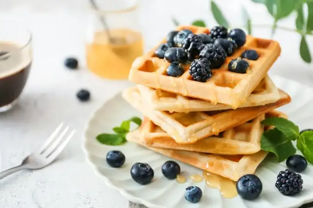 Stos gofrów z jagodami i miodem. Zastanawiasz się, ile kcal ma gofr? Ten deser wygląda pysznie!