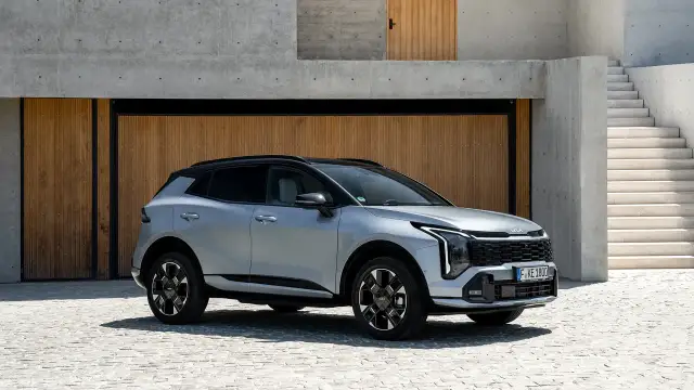 Srebrny Kia Sportage GT Line z czarnym dachem zaparkowany przed nowoczesnym budynkiem z drewnianymi drzwiami i betonowymi schodami.