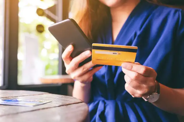 Frau hält Smartphone und goldene Kreditkarte für Online-Shopping.