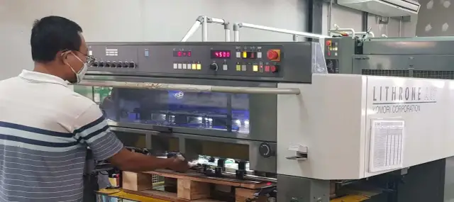 Operator w maszynie drukarskiej Komori Lithrone A37 z panelem sterowania i wyświetlaczem.