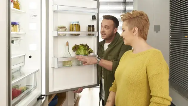 Para wybrać jaką lodówkę wybrać, para ogląda wnętrze z sałatą i przetworami.