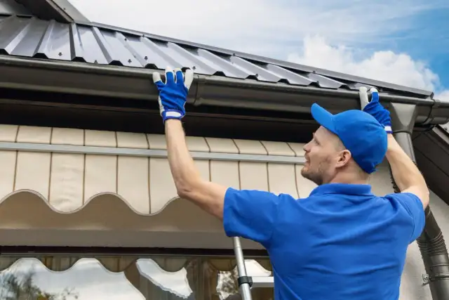 Mężczyzna w niebieskiej czapce i rękawiczkach montuje uszczelniacz do rynien plastikowych, dbając o szczelność dachu.