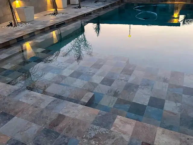 Escalones de baldosas de piedra entran en unas piscinas interiores, reflejando luces y árboles.